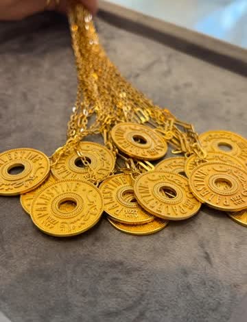 A hand holding a strand of gold lira-style coins over a grey cloth