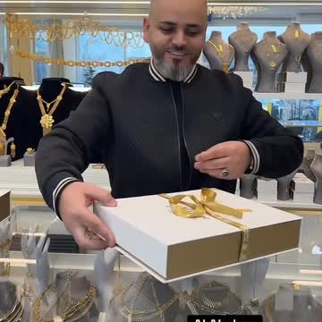 A white and gold gift box handed across the counter at Al Akaber Jewelry